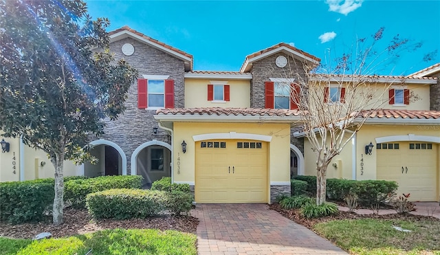 mediterranean / spanish-style house featuring a garage, stone siding, decorative driveway, and stucco siding