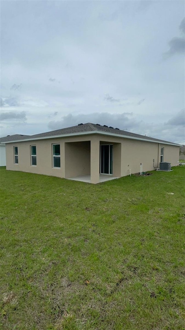 rear view of house featuring central air condition unit and a yard