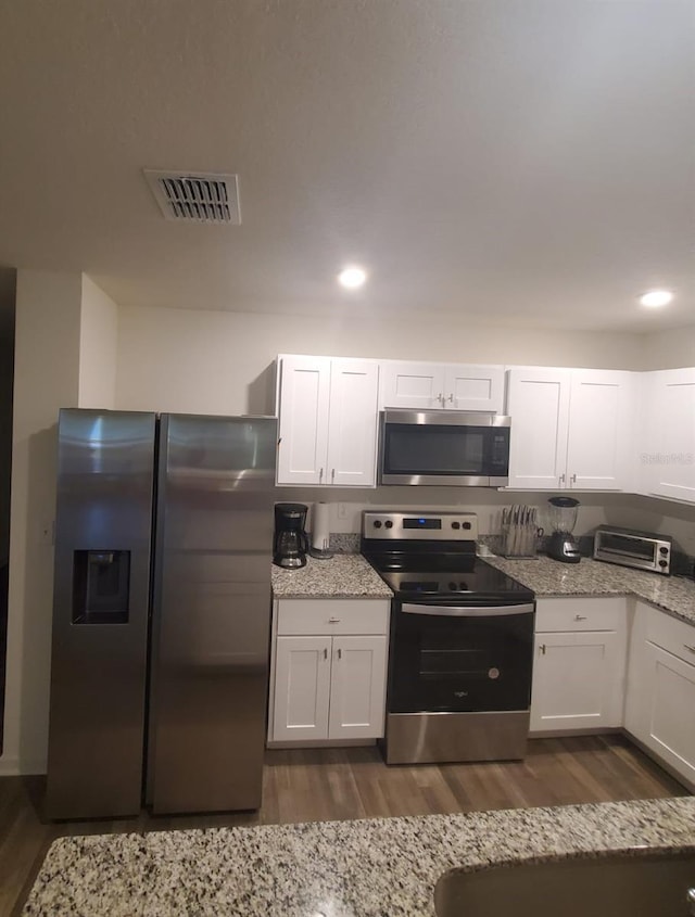 kitchen with light stone countertops, appliances with stainless steel finishes, dark hardwood / wood-style floors, and white cabinetry