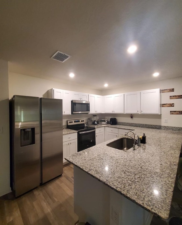 kitchen featuring kitchen peninsula, appliances with stainless steel finishes, dark hardwood / wood-style flooring, and white cabinets