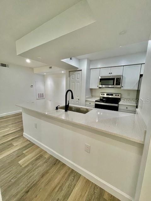 kitchen featuring kitchen peninsula, appliances with stainless steel finishes, light wood-type flooring, sink, and white cabinetry