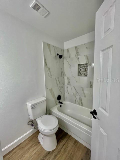 bathroom featuring toilet, tiled shower / bath combo, and hardwood / wood-style flooring