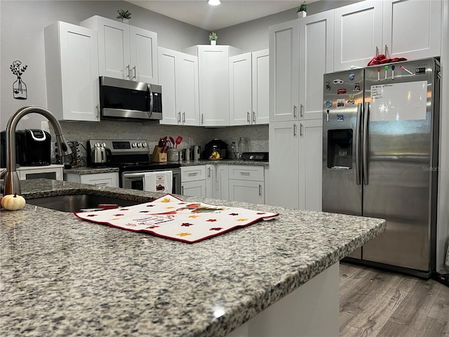 kitchen featuring light stone countertops, stainless steel appliances, white cabinetry, and light hardwood / wood-style floors