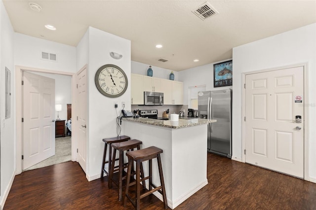 kitchen featuring kitchen peninsula, light stone countertops, appliances with stainless steel finishes, white cabinetry, and a breakfast bar area