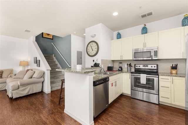 kitchen featuring a breakfast bar area, kitchen peninsula, light stone counters, and stainless steel appliances