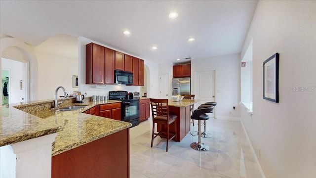 kitchen featuring kitchen peninsula, light stone counters, a breakfast bar, sink, and black appliances