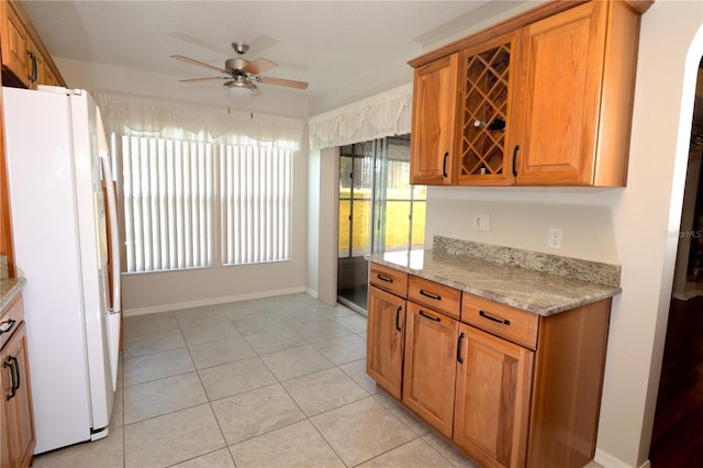 kitchen with white refrigerator, ceiling fan, light stone counters, and light tile patterned floors