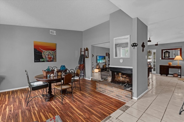 dining room with a textured ceiling, light wood-type flooring, a brick fireplace, and lofted ceiling