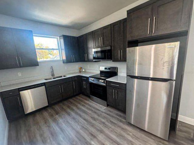 kitchen featuring wood-type flooring, appliances with stainless steel finishes, dark brown cabinetry, and sink