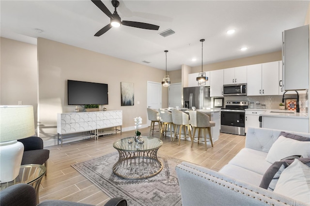 living room featuring ceiling fan, sink, and light wood-type flooring