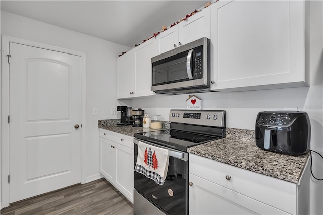 kitchen with white cabinetry, appliances with stainless steel finishes, dark hardwood / wood-style flooring, and dark stone counters