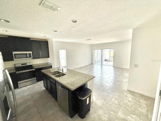 kitchen featuring sink, appliances with stainless steel finishes, light stone countertops, an island with sink, and a textured ceiling