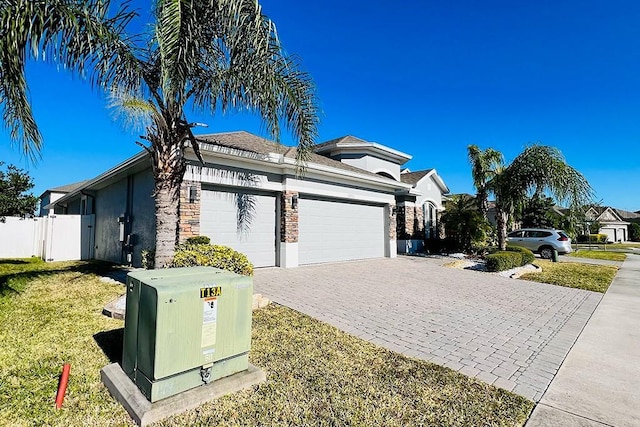 view of front of home featuring stucco siding, a front lawn, decorative driveway, fence, and an attached garage