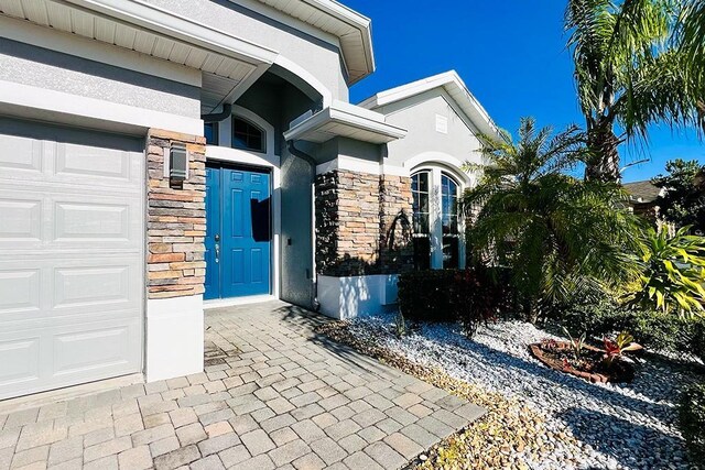 doorway to property with stucco siding, stone siding, and a garage