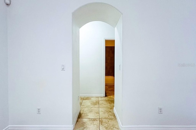 hall featuring light tile patterned floors, baseboards, and arched walkways