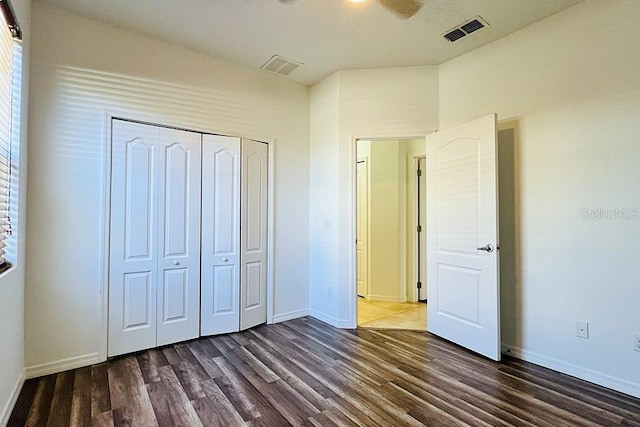 unfurnished bedroom with dark wood finished floors, baseboards, visible vents, and a closet