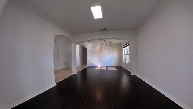 empty room featuring wood finished floors, visible vents, arched walkways, and ornamental molding