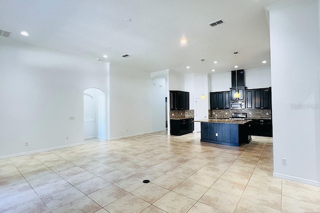 kitchen featuring arched walkways, open floor plan, stainless steel microwave, and a kitchen island with sink