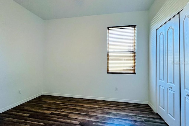 unfurnished bedroom featuring a closet, baseboards, and dark wood-style flooring