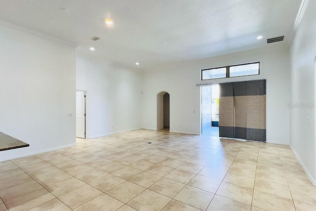 spare room with visible vents, baseboards, light tile patterned flooring, arched walkways, and a textured ceiling