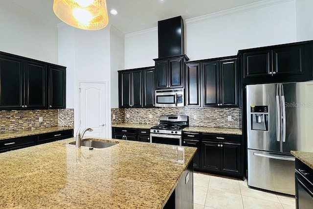 kitchen featuring light stone countertops, ornamental molding, dark cabinetry, stainless steel appliances, and a sink