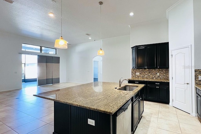 kitchen with arched walkways, dishwasher, dark cabinetry, and a sink