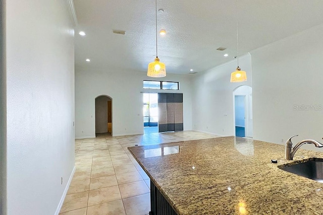 kitchen with arched walkways, decorative light fixtures, light stone countertops, and a sink