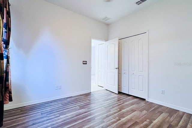 unfurnished bedroom with visible vents, wood finished floors, baseboards, and a closet