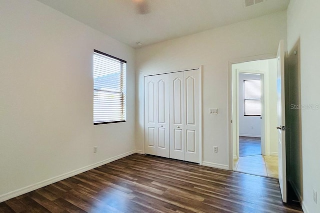 unfurnished bedroom featuring visible vents, dark wood-style floors, a closet, and baseboards