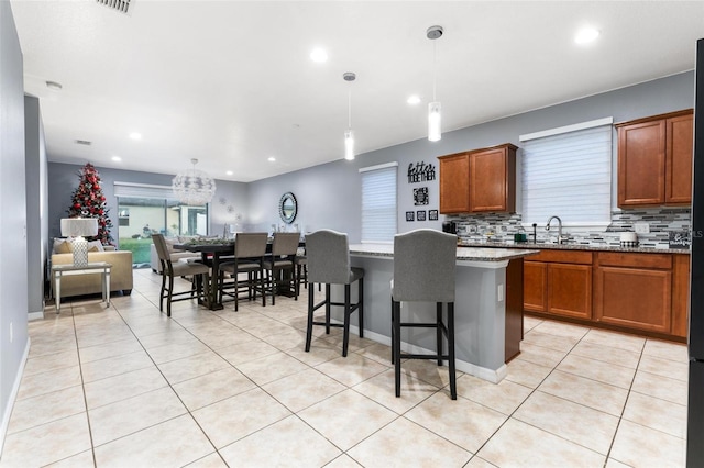 kitchen featuring backsplash, light stone counters, a breakfast bar, a center island, and hanging light fixtures