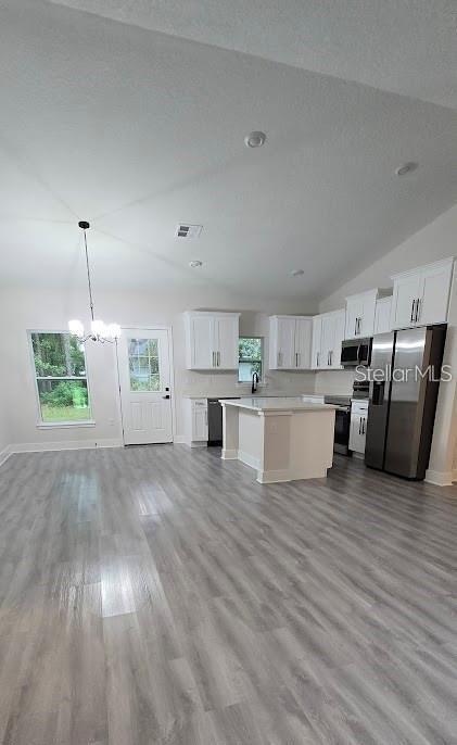 kitchen featuring pendant lighting, white cabinets, vaulted ceiling, a kitchen island, and stainless steel appliances