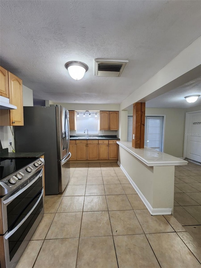 kitchen with stainless steel electric stove, sink, a textured ceiling, light tile patterned flooring, and kitchen peninsula