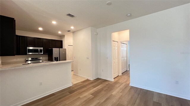 kitchen with light wood-type flooring, a textured ceiling, and appliances with stainless steel finishes