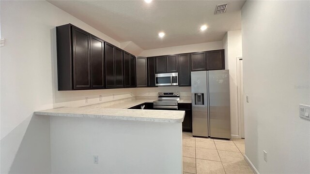 kitchen featuring kitchen peninsula, dark brown cabinets, light tile patterned floors, and appliances with stainless steel finishes