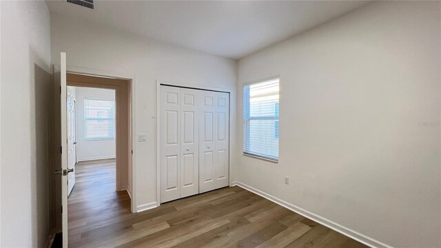 unfurnished bedroom featuring multiple windows, a closet, and hardwood / wood-style flooring