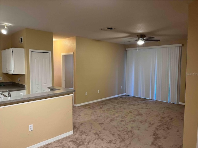 interior space featuring carpet, visible vents, baseboards, ceiling fan, and white cabinets