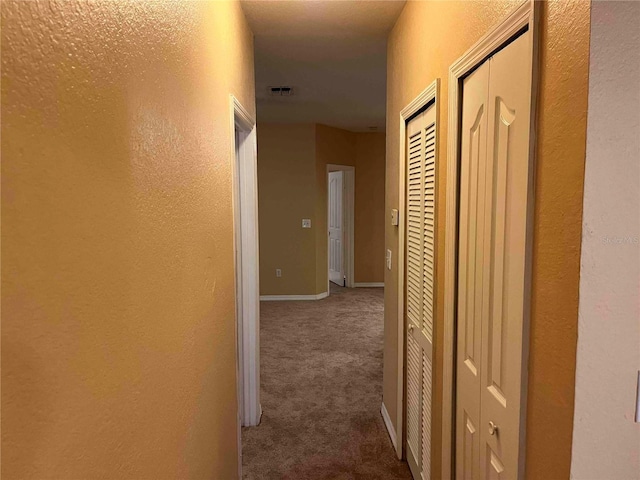 corridor featuring visible vents, dark colored carpet, a textured wall, and baseboards