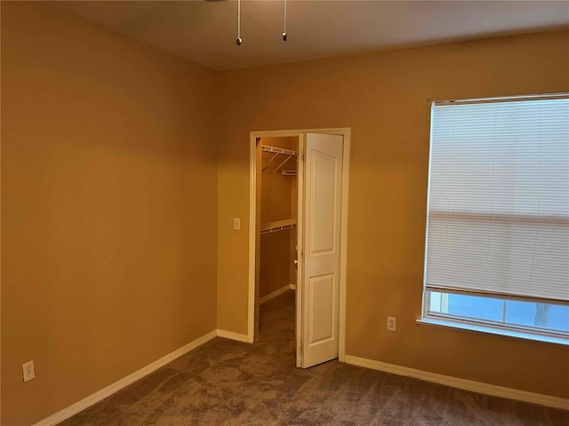 unfurnished bedroom with a spacious closet, a closet, baseboards, and dark carpet