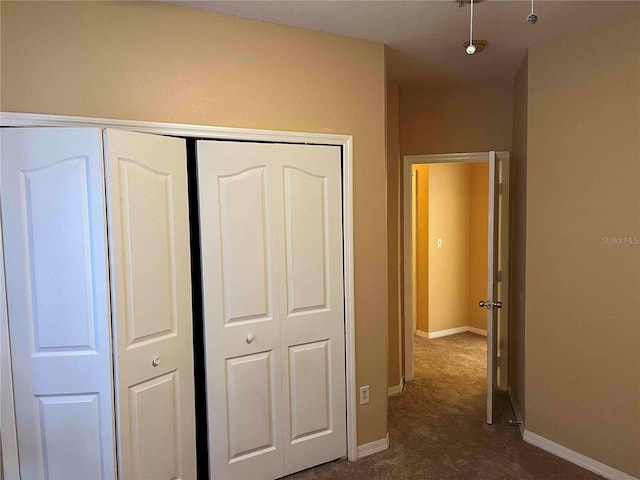 unfurnished bedroom featuring dark colored carpet, a closet, and baseboards