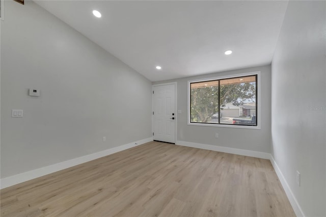 spare room featuring light wood-type flooring and vaulted ceiling