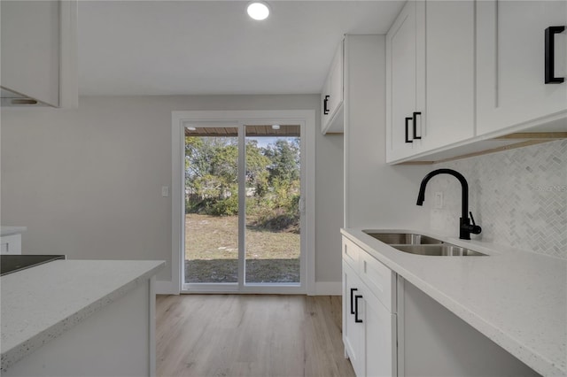 kitchen featuring backsplash, light stone counters, sink, white cabinets, and light hardwood / wood-style floors