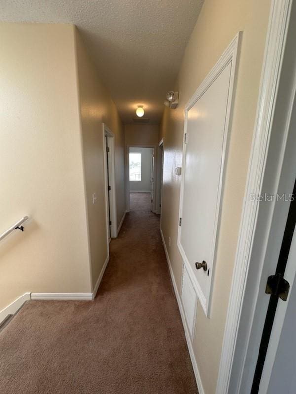 hall featuring carpet flooring and a textured ceiling