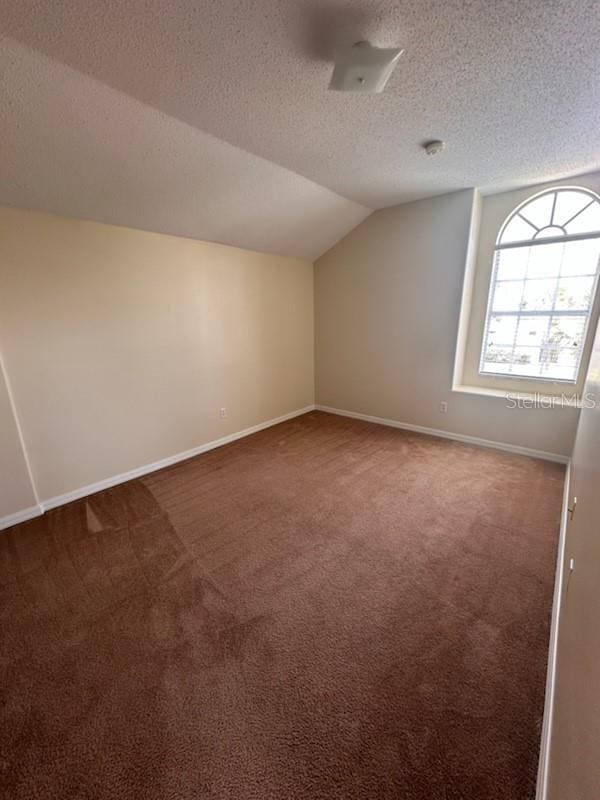 bonus room with dark colored carpet, lofted ceiling, and a textured ceiling