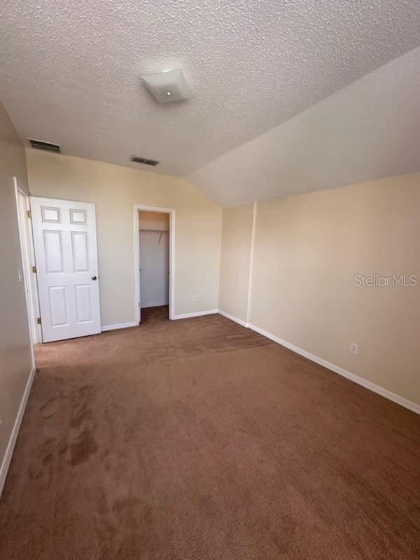 unfurnished bedroom featuring a spacious closet, lofted ceiling, a textured ceiling, a closet, and dark carpet