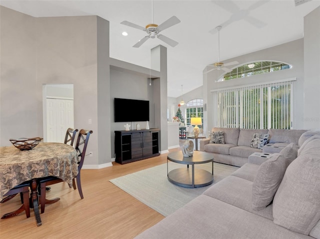 living room with a wealth of natural light, high vaulted ceiling, light hardwood / wood-style floors, and ceiling fan with notable chandelier