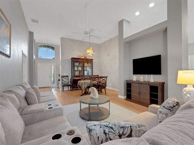 living room featuring ceiling fan, light hardwood / wood-style flooring, and a towering ceiling