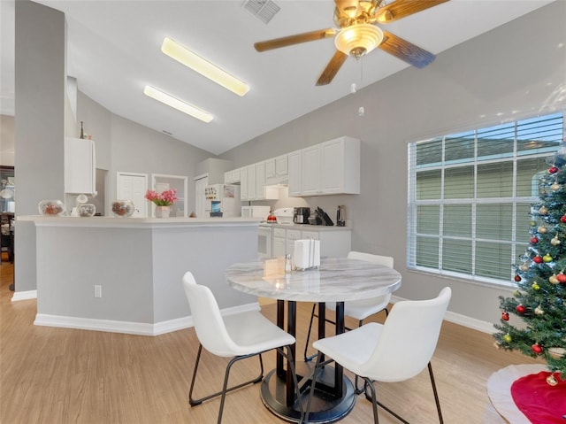 dining room with ceiling fan, vaulted ceiling, and light wood-type flooring