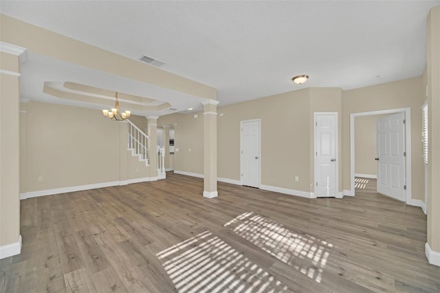 unfurnished living room with a raised ceiling, a chandelier, decorative columns, and light hardwood / wood-style floors