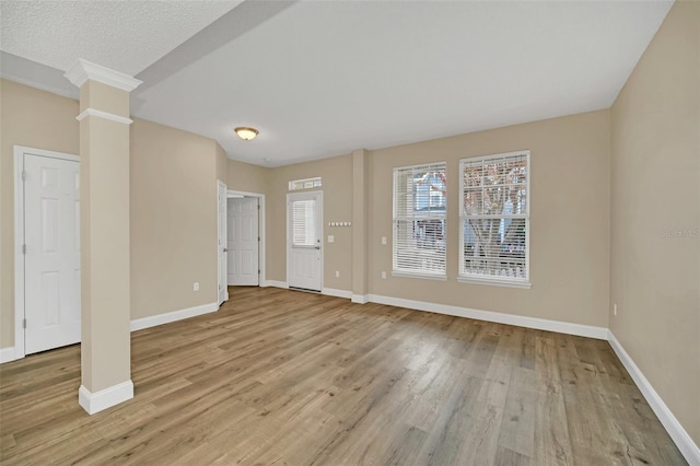 unfurnished room featuring a textured ceiling, decorative columns, and light hardwood / wood-style flooring