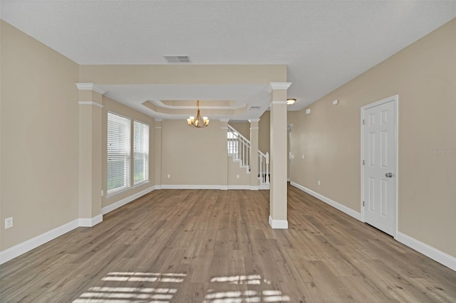 unfurnished living room featuring a chandelier, a textured ceiling, light wood-type flooring, and a tray ceiling